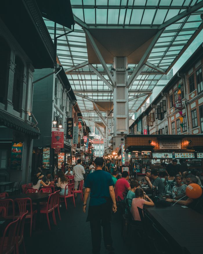 A bustling market scene in Singapores Chinatown with people dining and walking under a unique canopy.